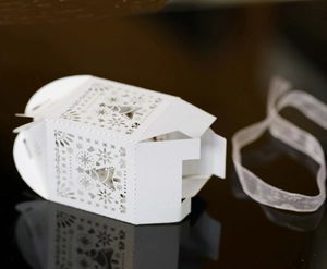 White laser-cut Christmas favor box with snowflake patterns and white ribbon