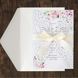 Laser cut hollow rose wedding invitation with ribbon bow on a rustic wood background