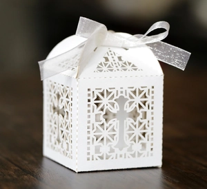 White laser cut cross hollow candy gift box with white ribbon bow on wood surface