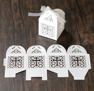 Laser-cut white cross pattern candy gift box with elegant white ribbon on dark wood