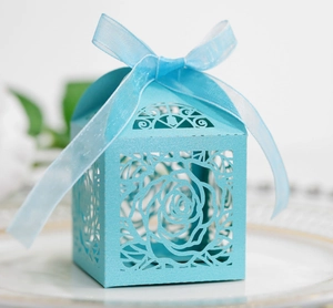 Sky blue laser-cut hollow rose candy box with silk ribbon bow on white ceramic plate