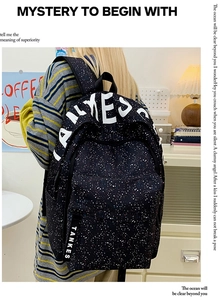 Close-up of black backpack with white star splatter pattern and woven TANKES side ribbon