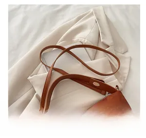 Detail view of brown suede handbag with leather strap and golden oval metal hardware