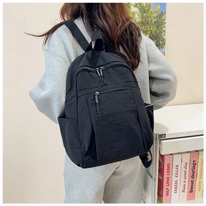 Rear view of model wearing a black water-resistant nylon backpack with multiple zippers