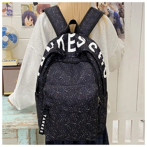 Detail of black backpack with white star texture and lettered straps worn by a person