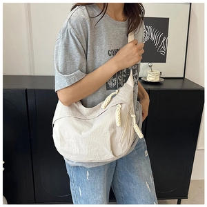 Détail du sac bandoulière beige en forme de croissant avec tirettes de fermeture tressées