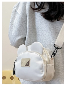 Close-up of cute bear ear detail and black metal hooks on the white canvas crossbody bag