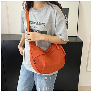 Détail du sac croissant en nylon orange avec large bandoulière porté par un mannequin