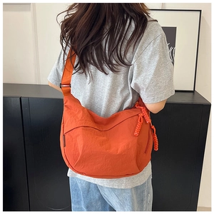 Vue arrière d'un mannequin portant un grand sac besace en nylon orange avec bandoulière tissée