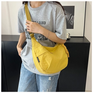 Détail d'un sac demi-lune jaune en nylon avec étiquette tissée noire et nœud de fermeture