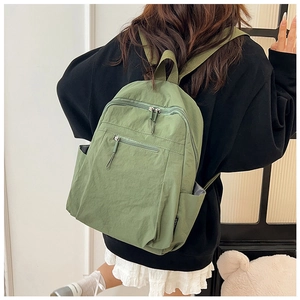 Rear view of a model wearing a green water-resistant nylon backpack with multi-pocket design