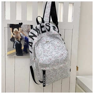Detailed view of TANKES canvas backpack with red and black splash pattern on white fence