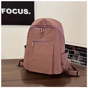 Detail view of water-resistant nylon backpack in dusty rose with multiple zipper pockets