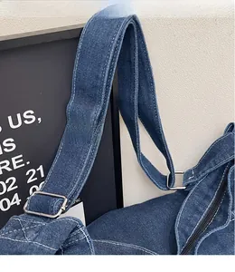 Détail de la bandoulière en denim réglable avec coutures blanches contrastées et boucle argentée