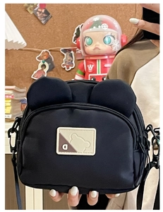 Detail shot of black nylon shoulder bag featuring cute 3D bear ears and a square logo patch