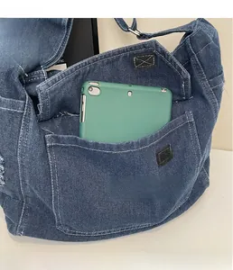 Détail du grand sac cabas en jean bleu montrant les poches et une tablette verte