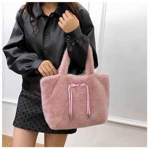 Pink plush tote bag with bow and tassel detail carried by a model on white background