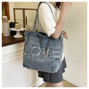 Detail of washed denim tote bag featuring frayed L.O.V.E letter patchwork and large capacity