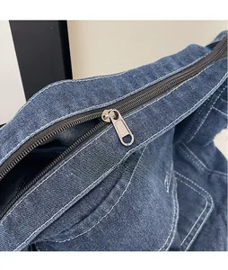 Détail d'un sac en denim bleu avec fermeture éclair en métal argenté mat et surpiqûres blanches