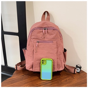 Medium-sized dusty pink nylon backpack with front pocket placed on a wooden surface