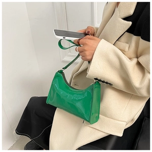 Détail du sac baguette en cuir verni vert vif porté avec un manteau en laine neutre