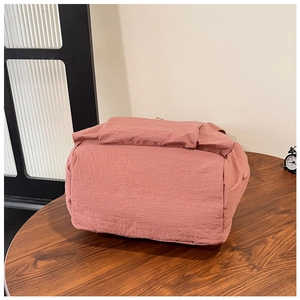 Detail view of water-resistant pink nylon backpack with flap closure on wooden table