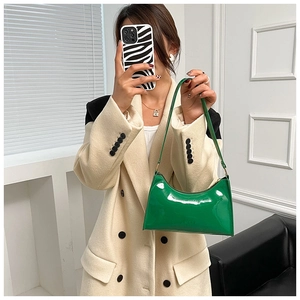 Détail d'un sac baguette en cuir verni vert vif porté avec un trench-coat de couleur crème