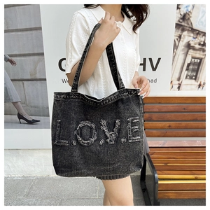 Detail of vintage washed denim tote bag featuring frayed LOVE patch on model's shoulder