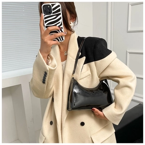 Chic sac sous le bras en cuir verni noir porté à l'épaule avec une veste de blazer