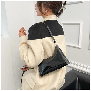 Gros plan du sac baguette en cuir verni noir porté à l'épaule avec un style minimaliste