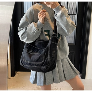 Détail du sac bandoulière en toile noire avec surpiqûres blanches et poche utilitaire