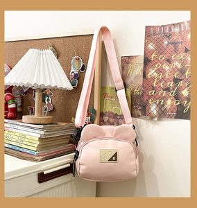 Detailed shot of pink bear-ear crossbody bag with adjustable strap in cozy room setting