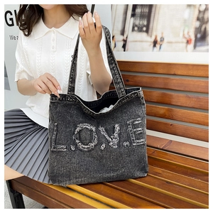 Detail of grey washed denim tote bag with frayed LOVE letter patchwork in casual outdoor setting