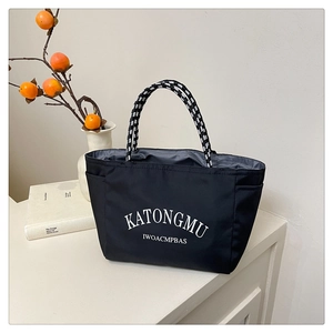 Detail of black nylon tote bag featuring white lettering and woven rope handles