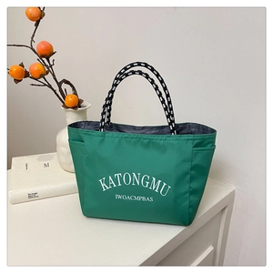 Detail of green nylon tote bag featuring striped woven handles and white letter printing