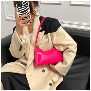 Détail d'un sac hobo en cuir verni magenta porté avec un blazer élégant