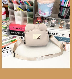 Detail showing cute bear ear design and durable nylon fabric on a beige crossbody bag