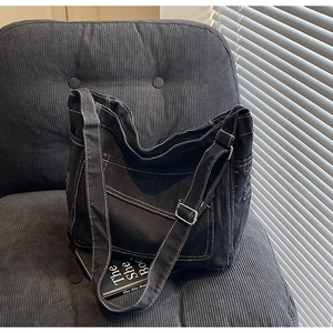 Détail d'un sac cabas en toile noire avec surpiqûres blanches et bandoulière réglable