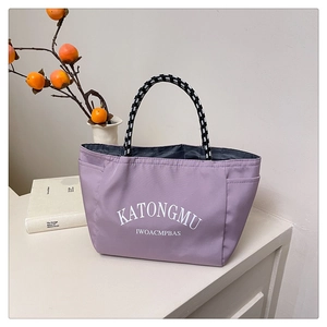 Detail view of purple nylon tote with woven handles and side pockets on a white desk