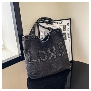 Detail of black denim tote bag featuring LOVE letter patch and frayed edge texture
