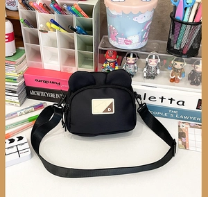 Detail of black nylon bear crossbody bag with cute ear design on a vibrant desk setup