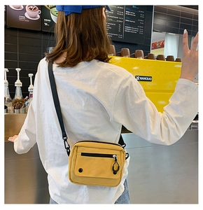 Detailed view of yellow canvas crossbody bag with adjustable black strap and zipper pocket