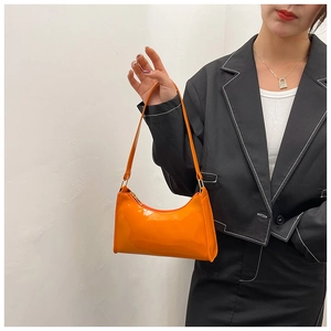 Détail d'un sac baguette en cuir verni orange brillant porté avec un blazer noir