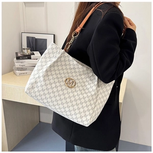 White tote bag with grey M pattern, brown leather strap and gold logo on a model