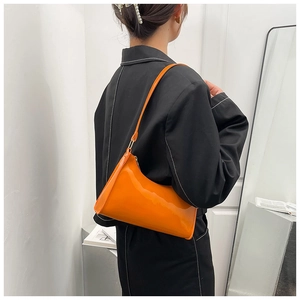 Détail du sac baguette orange brillant sur un blazer noir pour un style de mode moderne