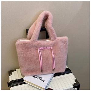 Detail of soft pink plush tote bag with tassel accent resting on a suitcase