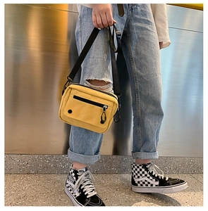 Detail of yellow canvas crossbody bag featuring functional zipper pocket and street style design