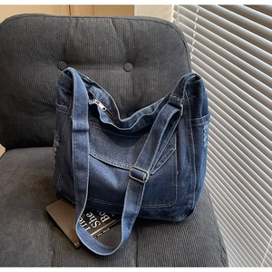 Détail du sac à bandoulière en jean avec bords effilochés sur une chaise en velours