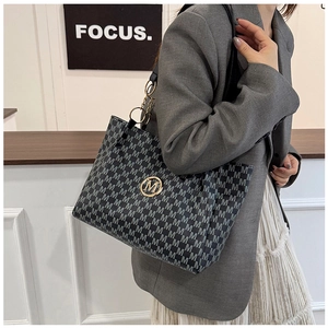 Detail of dark grey tote bag with M jacquard pattern and gold chain strap on model