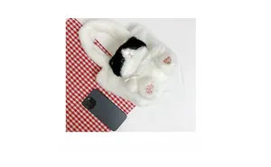 Close-up of white plush cat bucket bag with lace collar and heart nose detail next to phone
